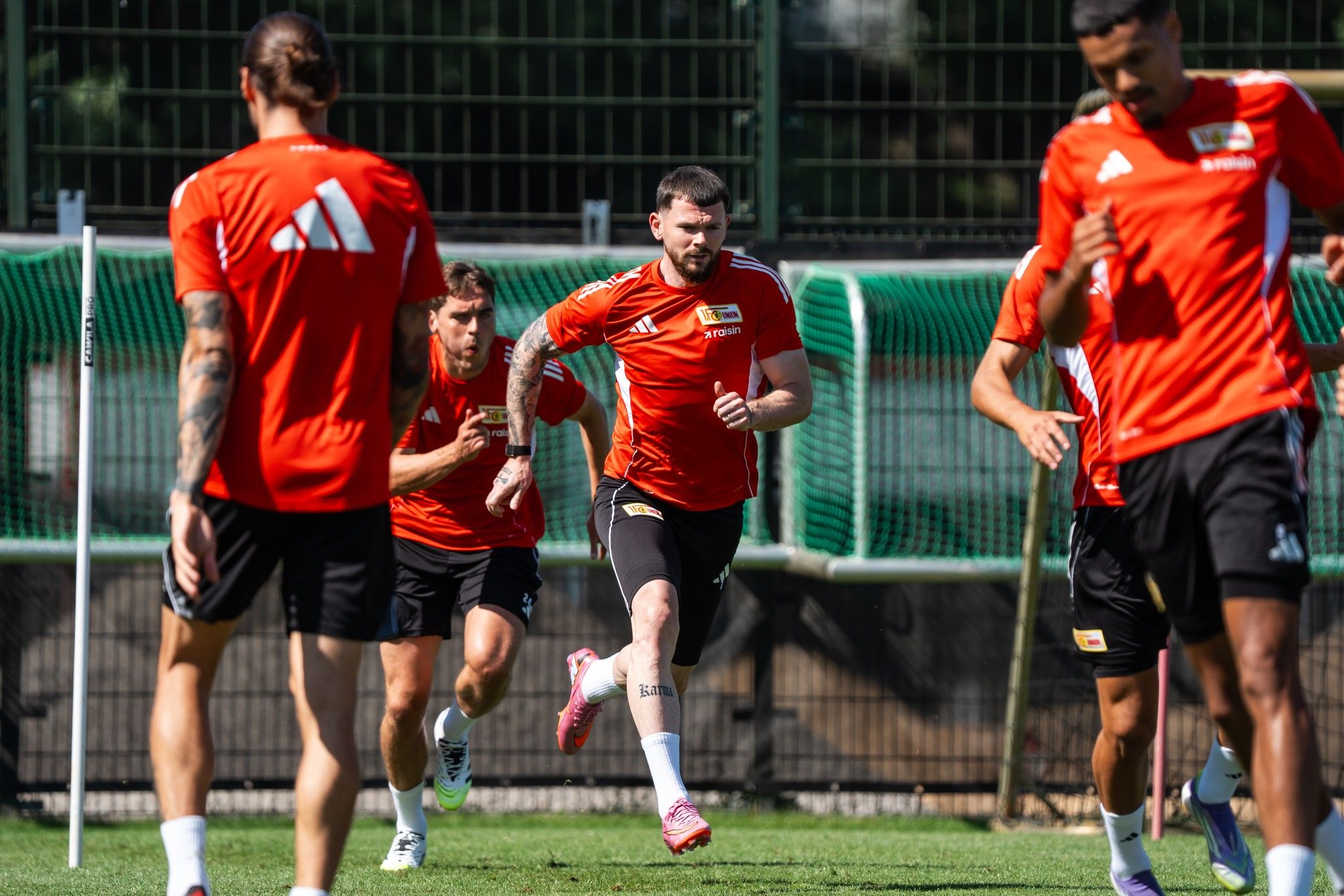 Fußballspieler in roten Trikots trainieren auf einem Rasenfeld, während sie sprinten und sich auf das Training konzentrieren.