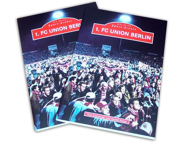 Zwei Bücher über den 1. FC Union Berlin, umgeben von Fans in einem Stadion, mit rotem Cover und Schriftzug.