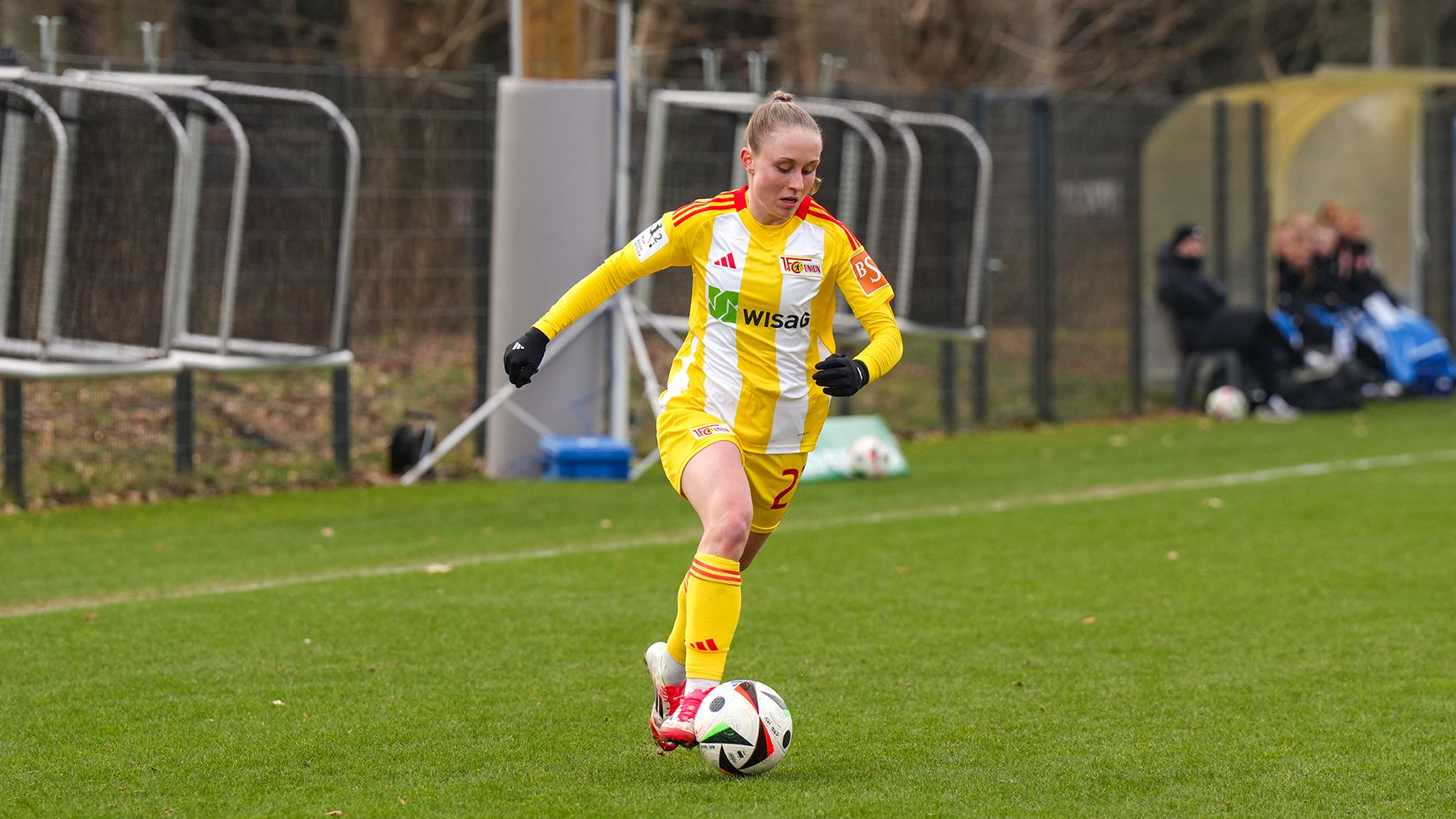 Eine Fußballspielerin in gelb-weißem Trikot dribbelt den Ball auf einem Kunstrasenplatz.
