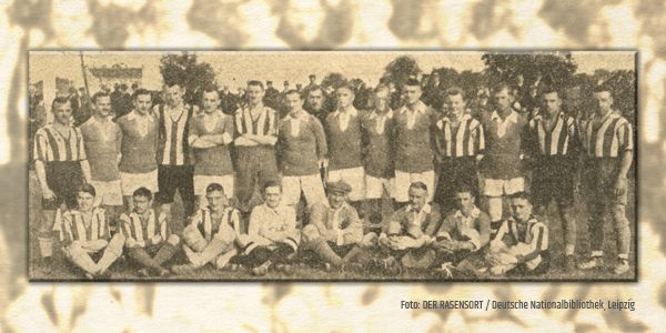 Schwarz-weißes Foto einer Fußballmannschaft mit Spielern in gestreiften und einfarbigen Trikots, auf einer Wiese stehend und sitzend.