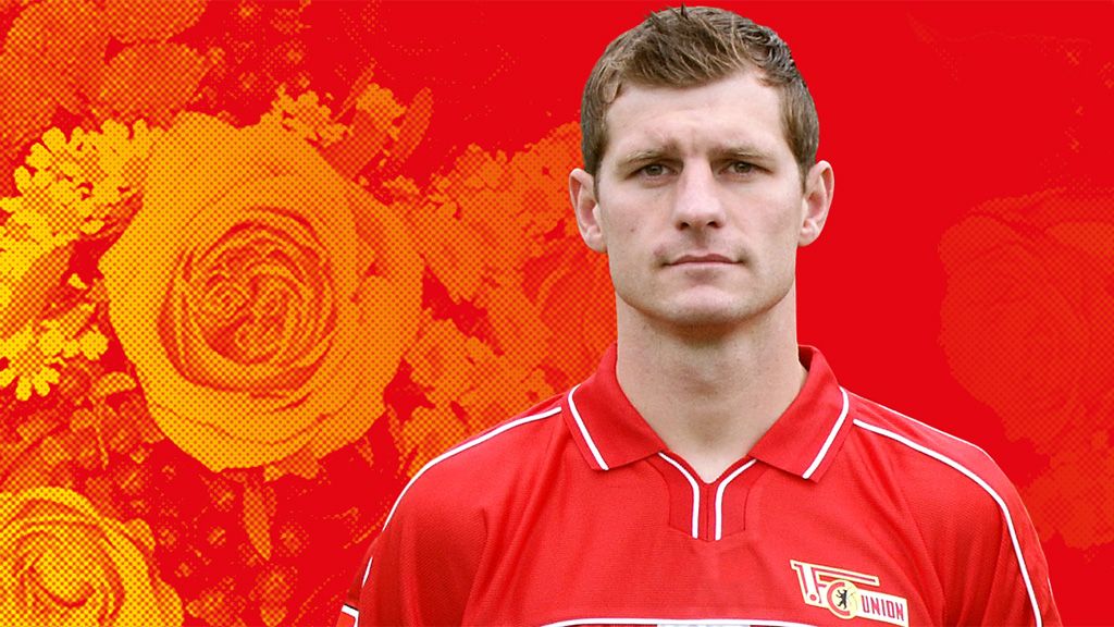 Ein männlicher Fußballspieler in rotem Trikot steht vor einem orange-roten Hintergrund mit stilisierten Blumen.