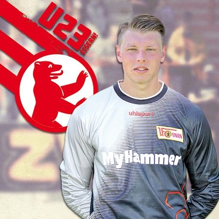 Ein sportlicher junger Mann in einem grauen Fußballtrikot, steht vor einem Logo mit einem roten Bären und der Aufschrift "U23".