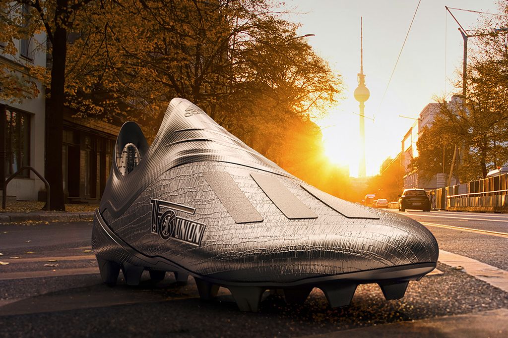 Ein überdimensionaler Fußballschuh steht auf einer Straße, mit einem Sonnenuntergang und Stadthintergrund im Hintergrund.