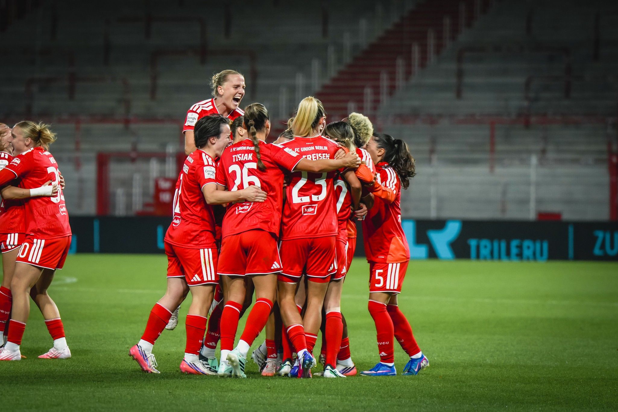 Mannschaft von Frauenfußballspielerinnen in roten Trikots feiert einen Treffer auf dem Spielfeld.