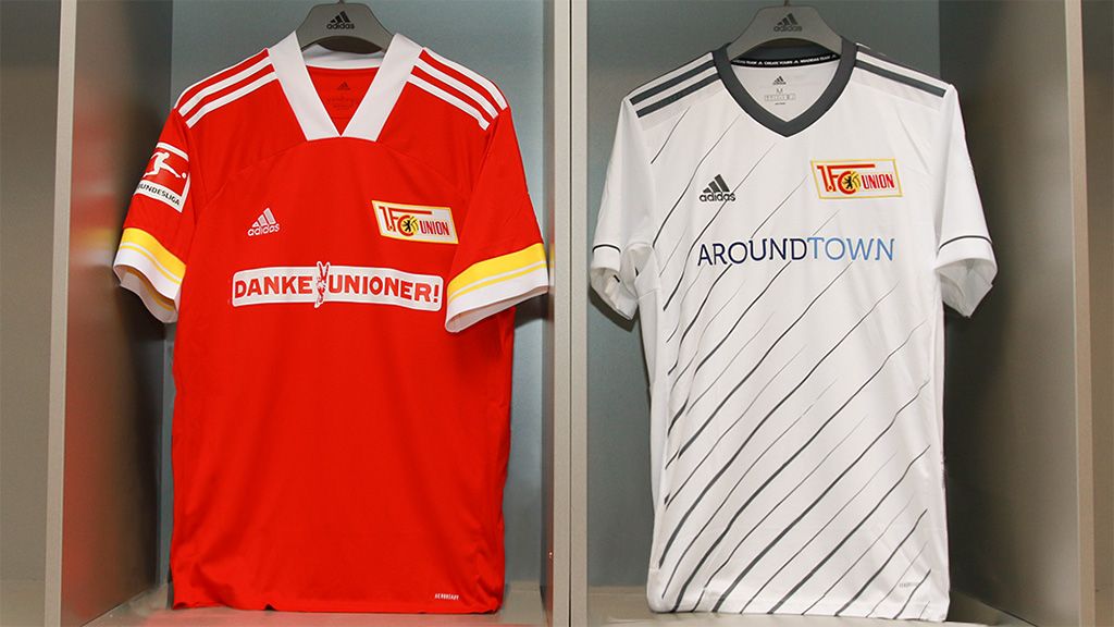Zwei Fußballtrikots des 1. FC Union Berlin: ein rotes Heimtrikot und ein weißes Auswärtstrikot, jeweils mit Sponsorenlogo und Adidas-Branding.