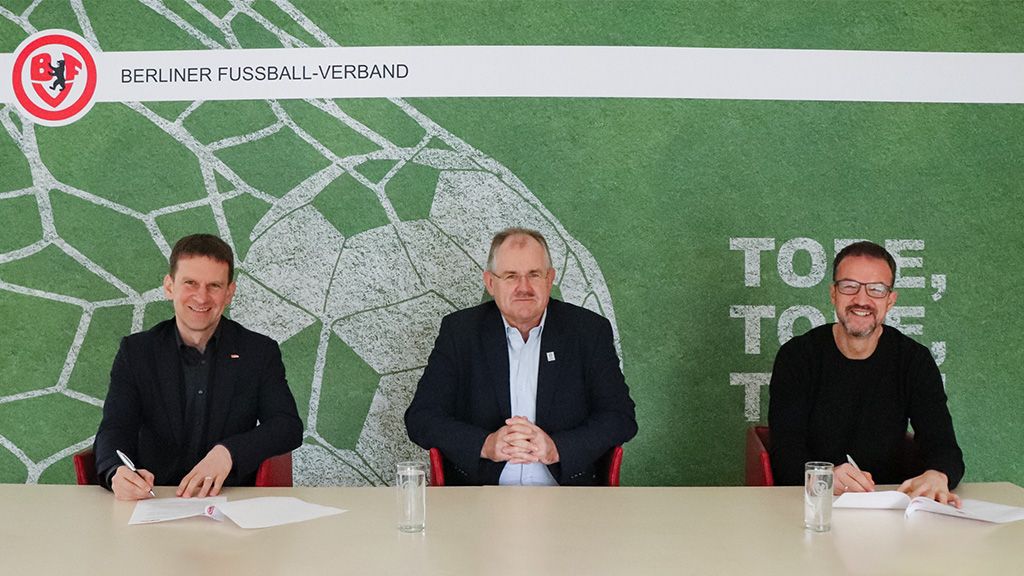 Drei Männer sitzen an einem Tisch vor einer grünen Fußball-Hintergrundwand, mit dem Logo des Berliner Fußball-Verbandes im Hintergrund.