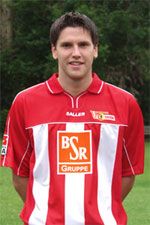 Ein junger Mann in einem roten und weißen Fußballtrikot steht vor einem grünen Hintergrund.