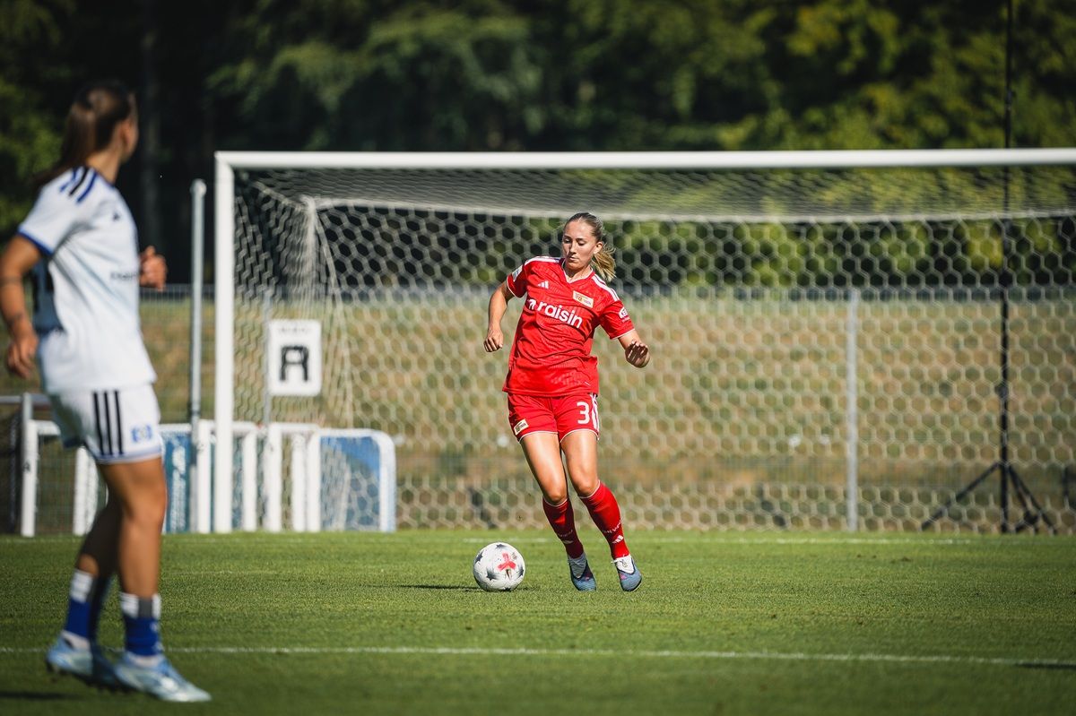 Eine Fußballspielerin in roter Uniform dribbelt den Ball auf einem grünen Spielfeld vor dem Tor.