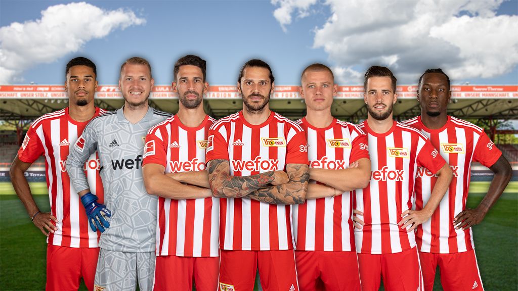 Eine Gruppe von sieben Fußballspielern in rot-weiß gestreiften Trikots steht auf einem Stadionfeld vor einer Stadionhintergrund.