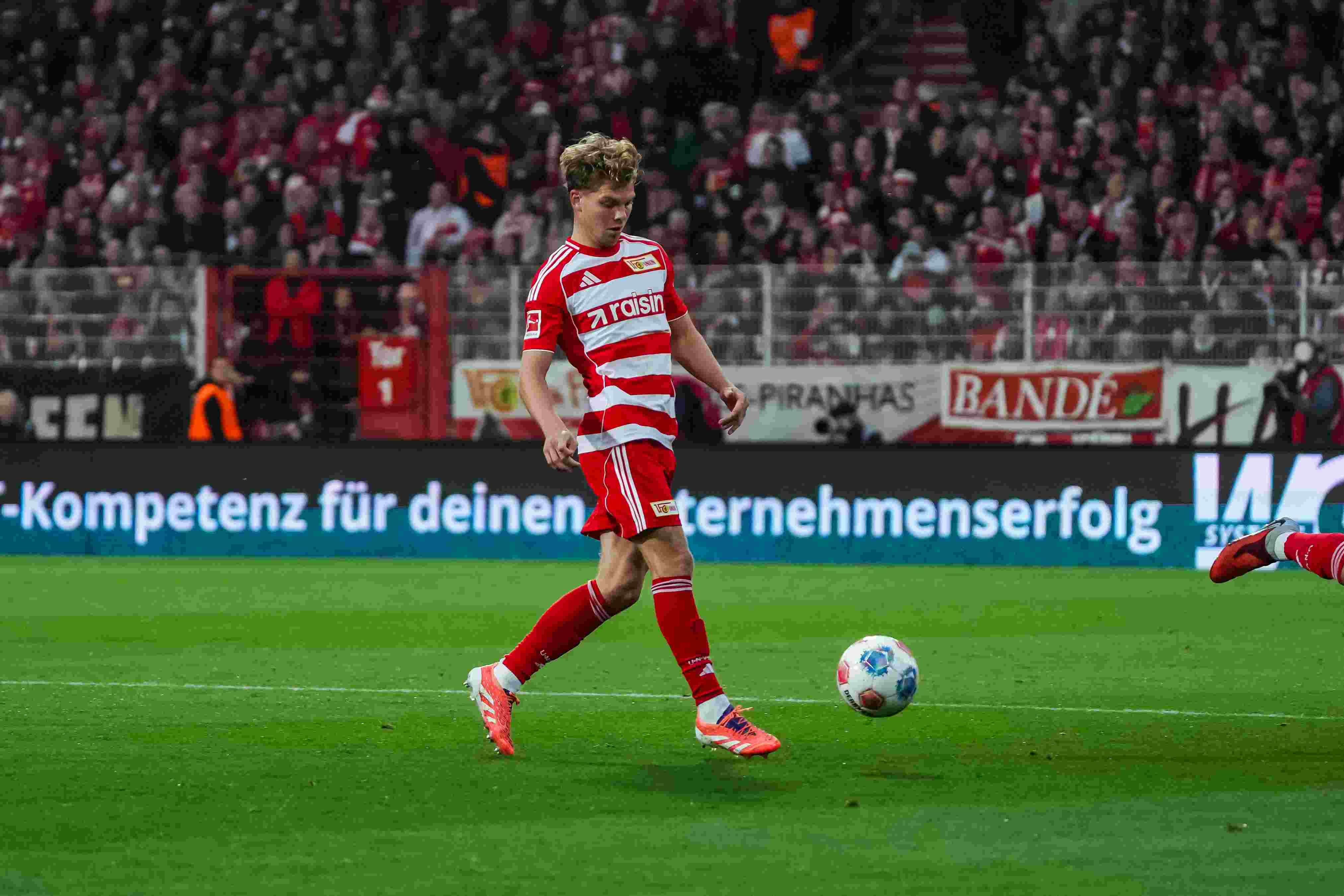 Ein Fußballspieler in rot-weißer Uniform steht auf dem Spielfeld und bereitet sich darauf vor, den Ball zu treten.