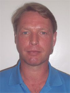 Mann mit blonden Haaren, trägt ein blaues Hemd, vor einem einfarbigen Hintergrund.