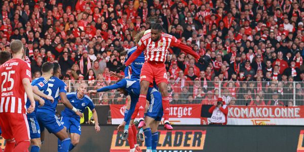 Game scene in the stadium: A player in red and white uniform jumps high, while other players in blue jerseys try to prevent him.