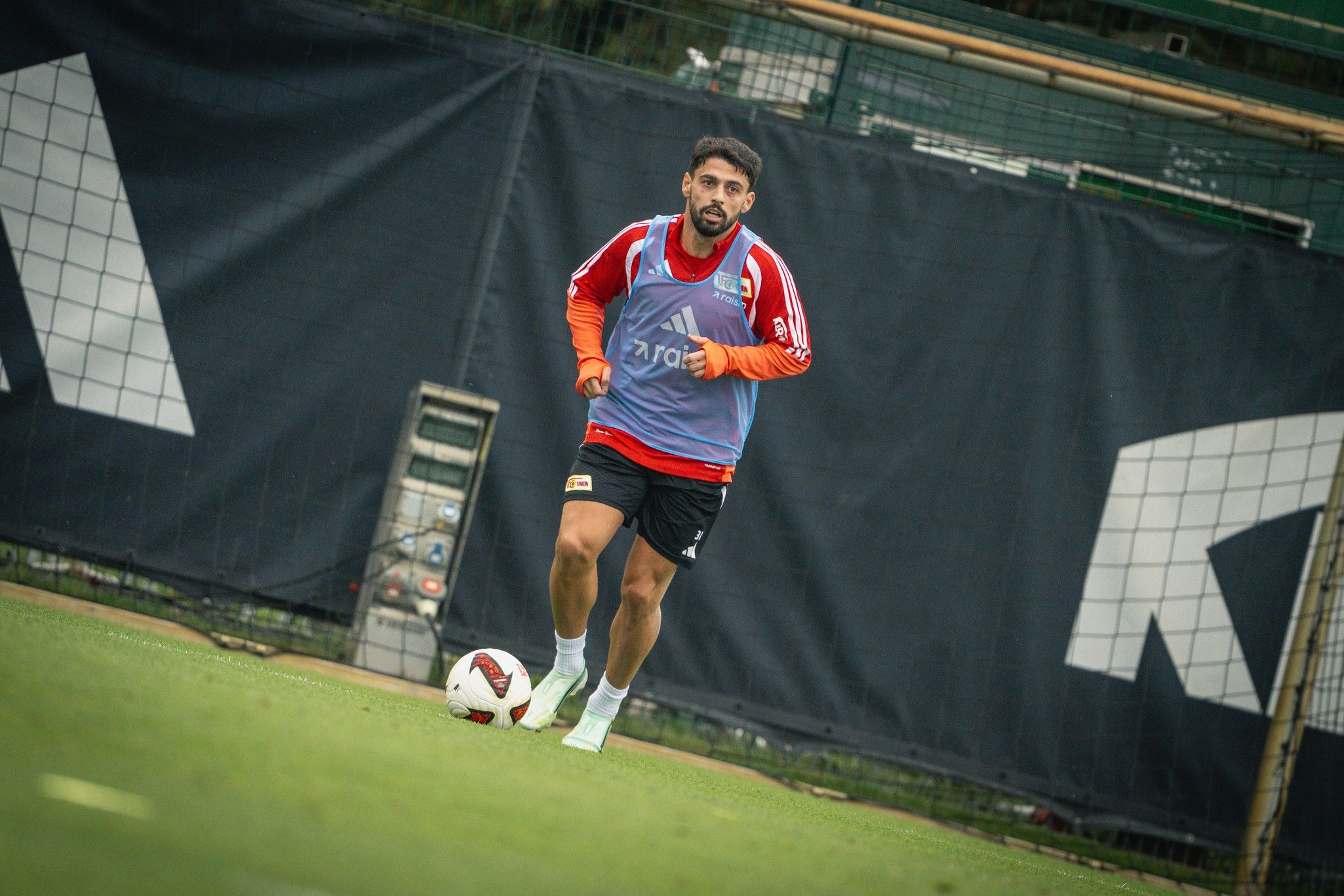 Fußballspieler in Trainingskleidung läuft über das Feld, umgeben von Toren und einem Trainingsgelände.