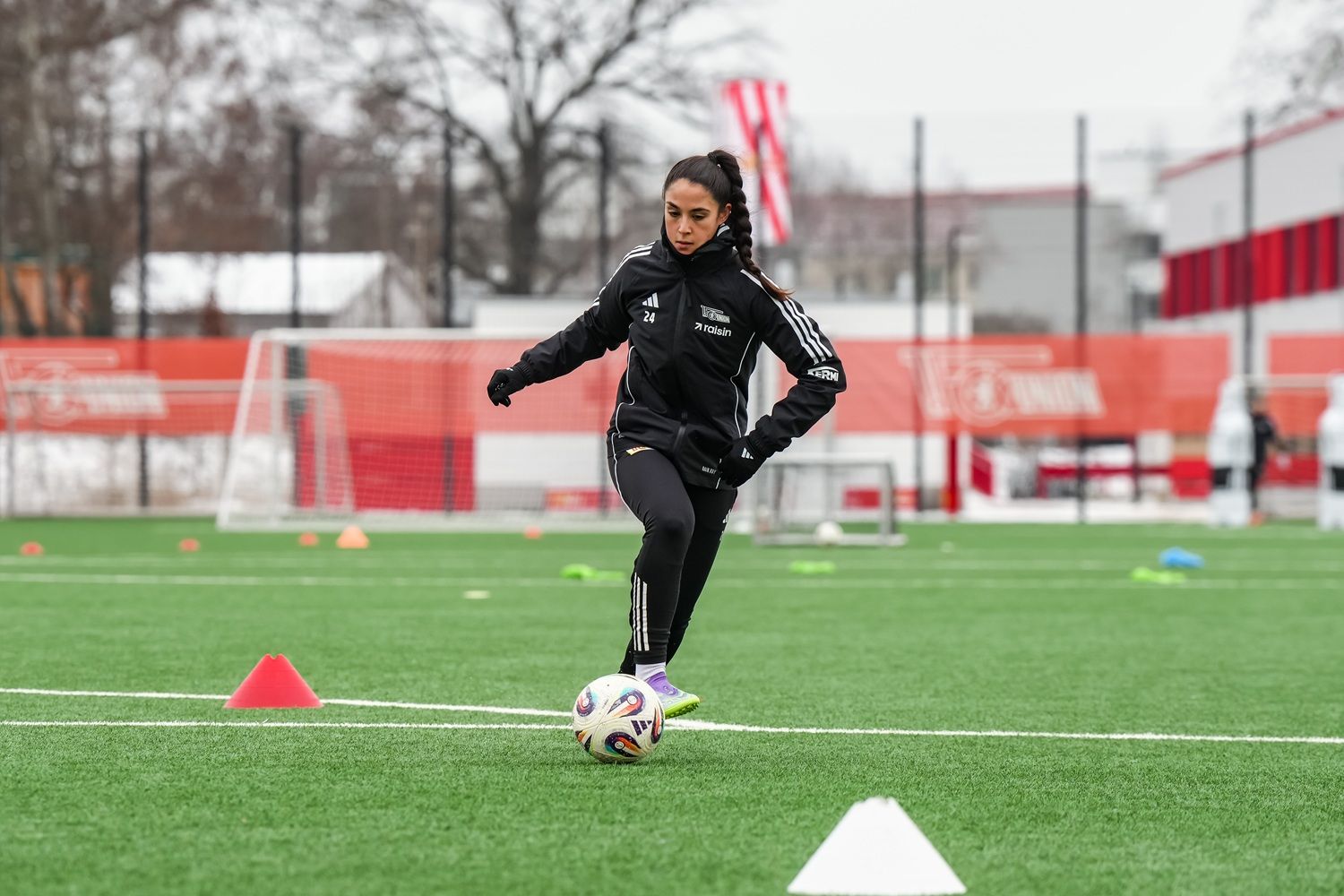 Eine Fußballspielerin dribbelt den Ball auf einem Trainingsplatz, umgeben von Hütchen und weiteren Trainingsmaterialien.