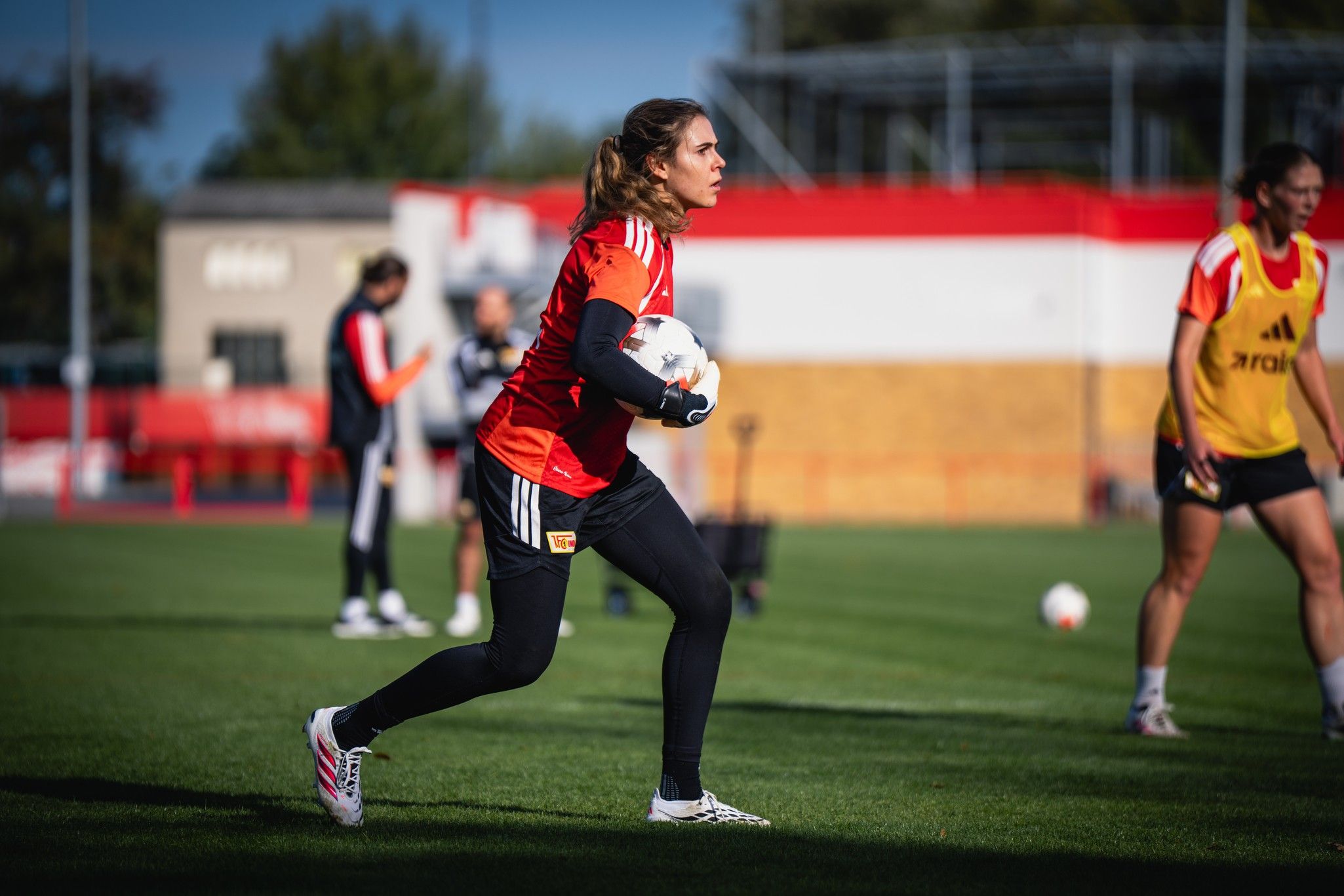 Eine Fußballspielerin trainiert auf dem Platz, hält den Ball in den Händen und richtet sich auf das Spielgeschehen aus.