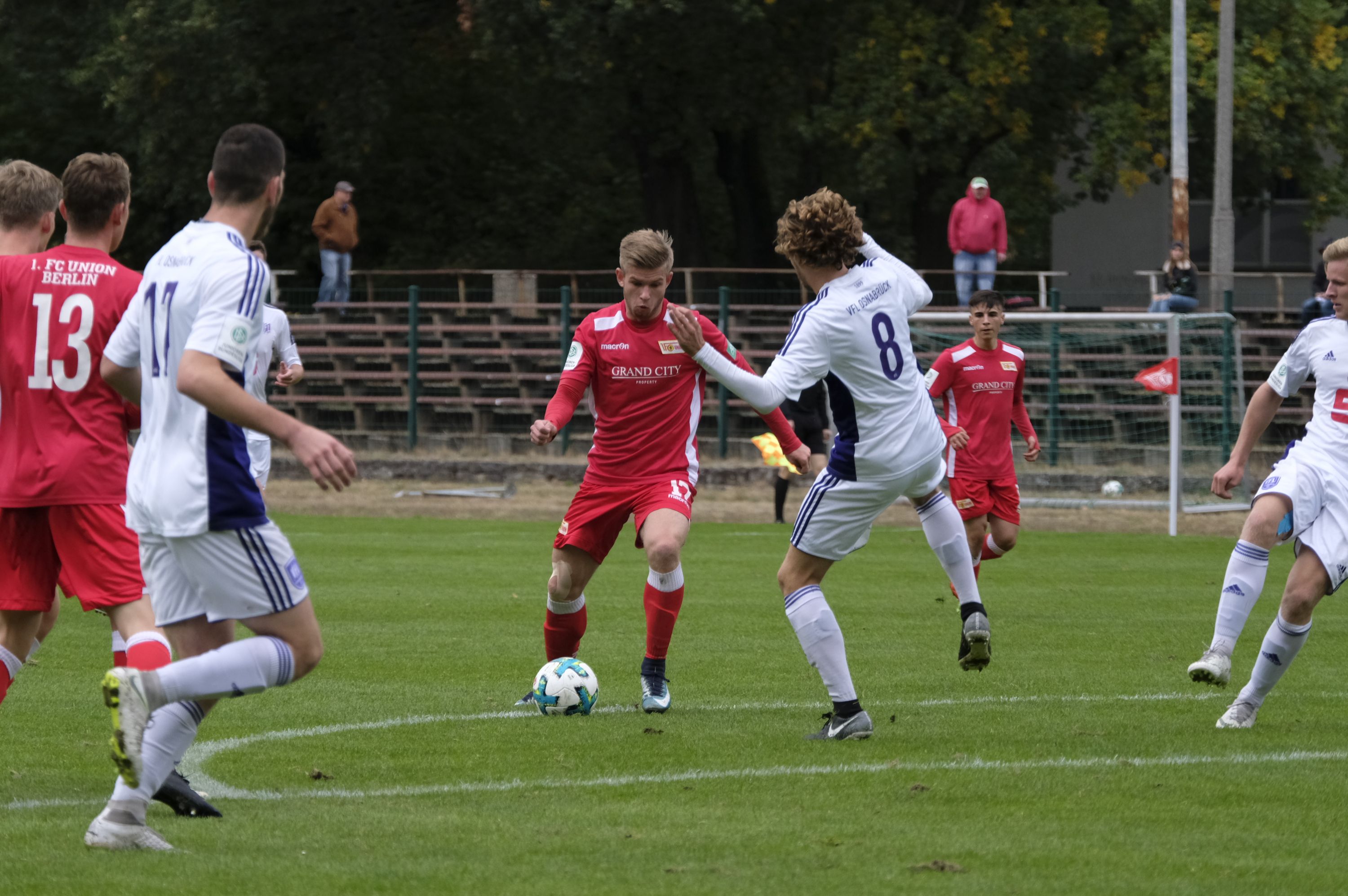 A soccer game with two teams in red and white jerseys. A player dribbles the ball while an opponent tries to stop him.