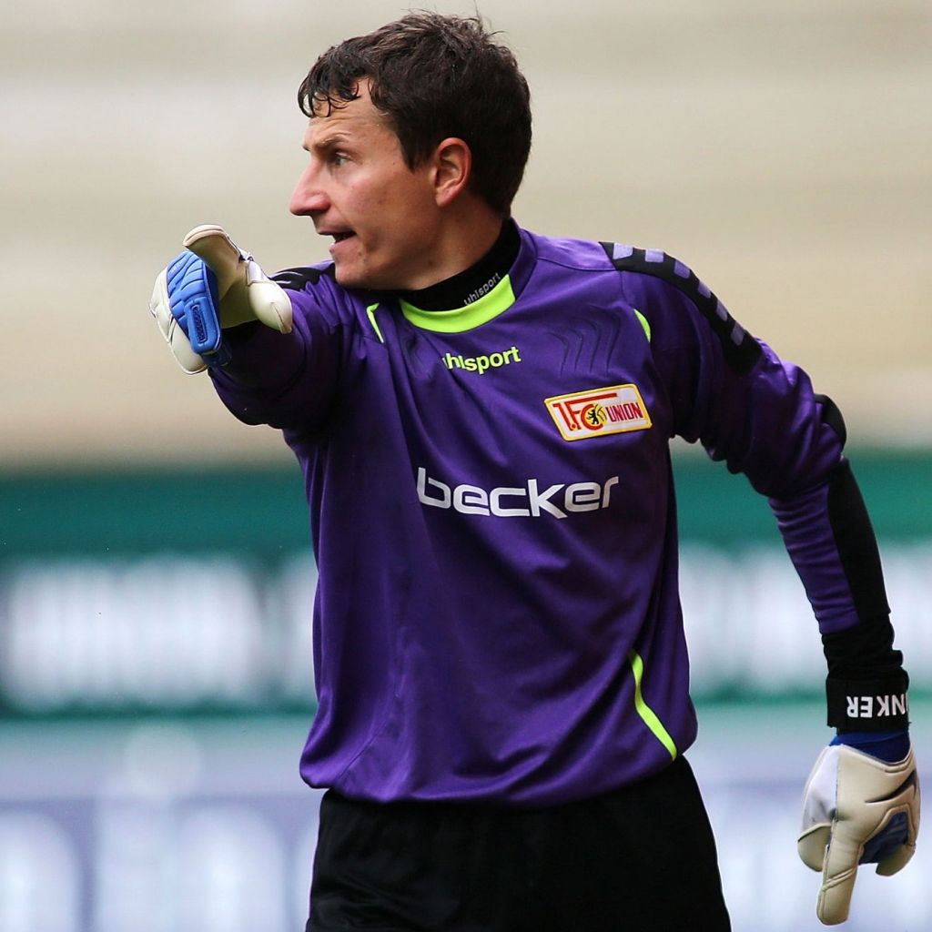 Torhüter in lilafarbenem Trikot mit aufgestütztem Arm, deutet auf das Spielfeld.