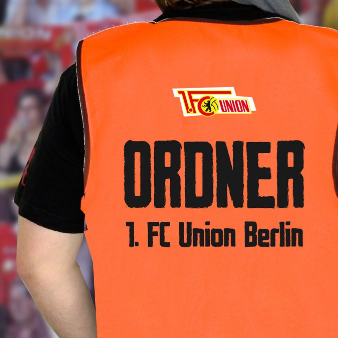 Oranger Weste eines Ordners mit der Aufschrift „ORDNER 1. FC Union Berlin“ auf dem Rücken.