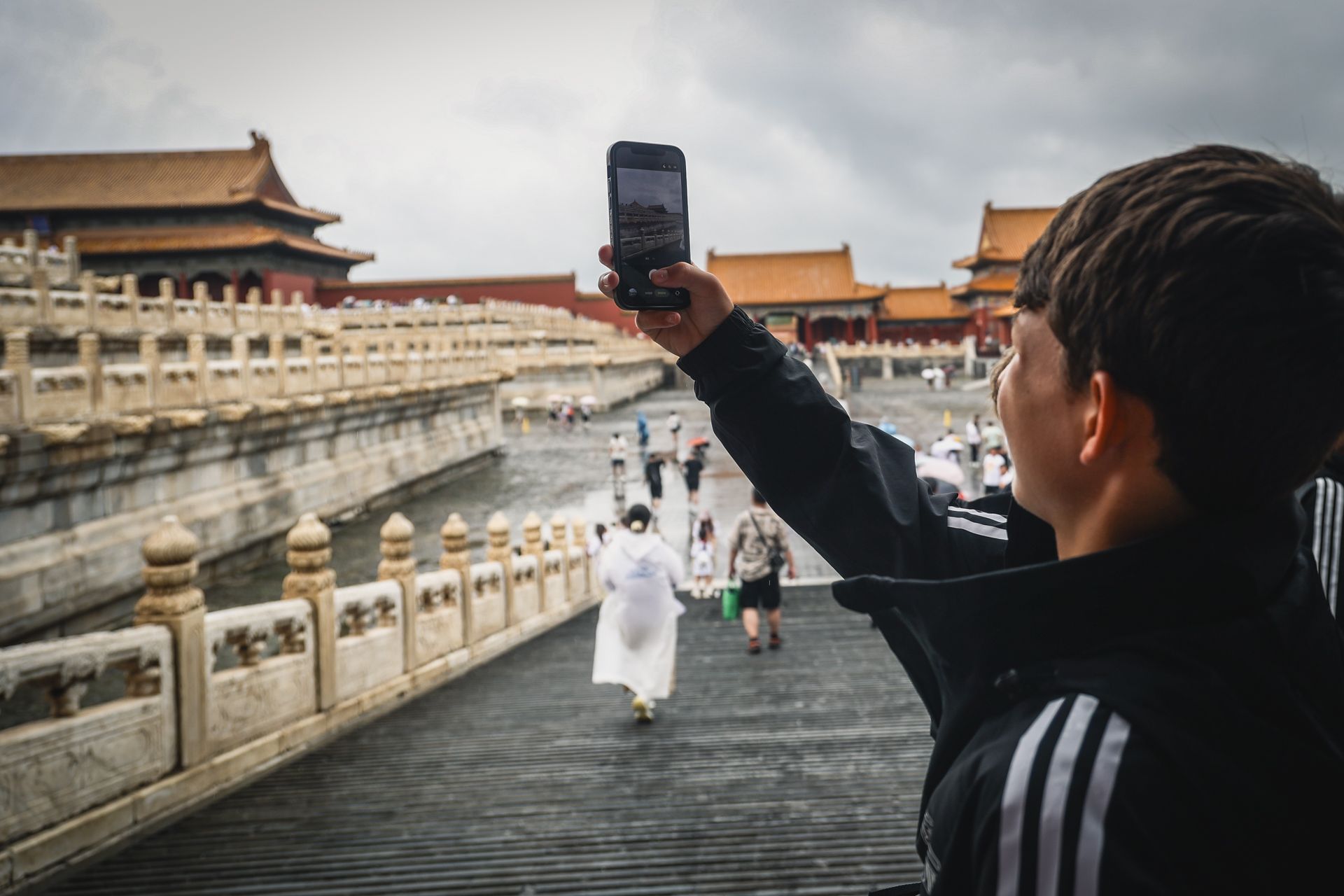 Ein Junge hält ein Smartphone in die Höhe und fotografiert die Umgebung in einer historischen Stätte mit Menschen und traditioneller Architektur.