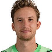 Ein junger Mann mit kurzen, lockigen Haaren lächelt in einem grünen Fußballtrikot vor einem neutralen Hintergrund.