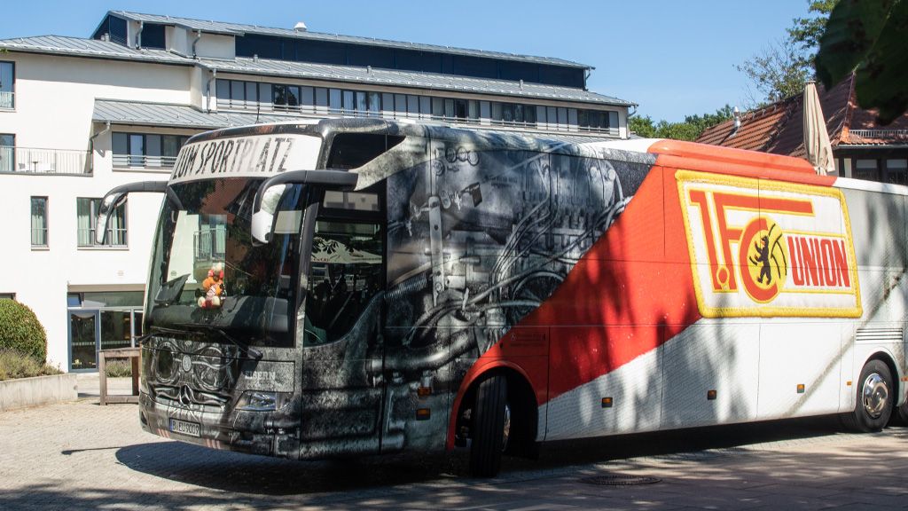 Ein Bus mit künstlerischer Bemalung und dem Logo eines Fußballvereins steht vor einem modernen Gebäude.
