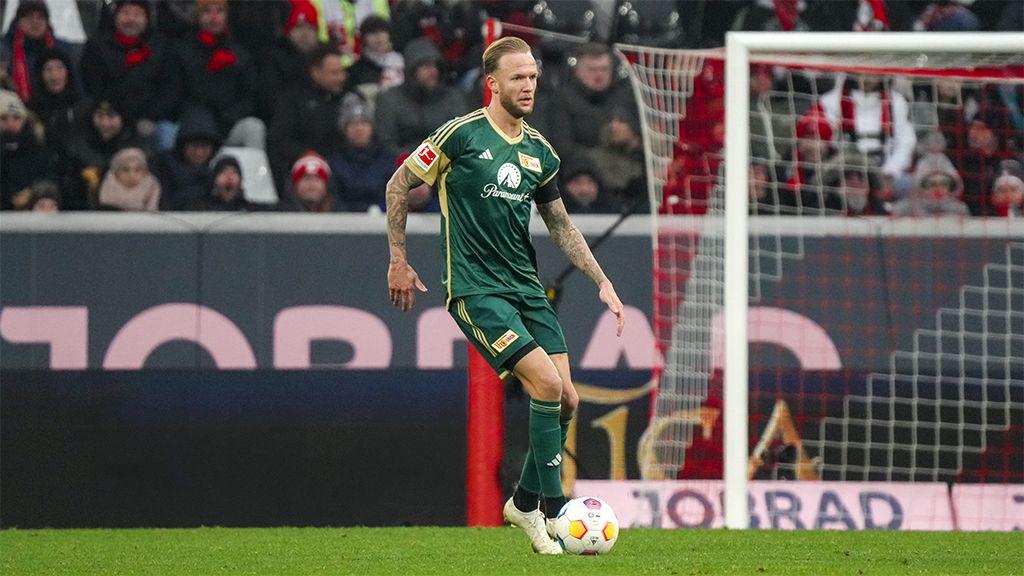 A soccer player in green gear is dribbling the ball on the field, with fans in the background.