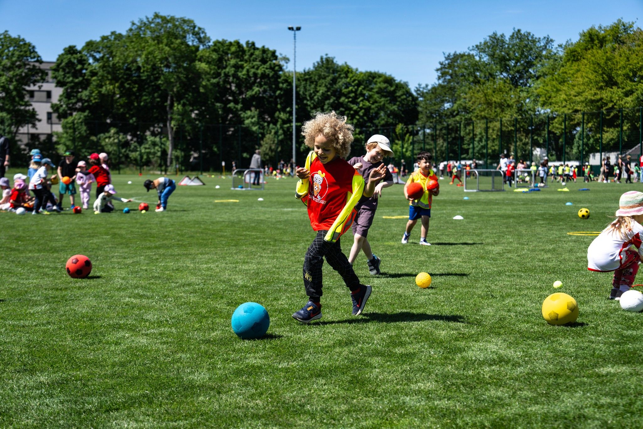 Kinder spielen auf einer Wiese mit bunten Bällen an einem sonnigen Tag.