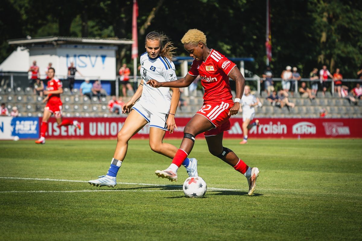 Zwei weibliche Fußballspielerinnen in Aktion auf dem Spielfeld, eine in rotem und die andere in weißem Trikot.