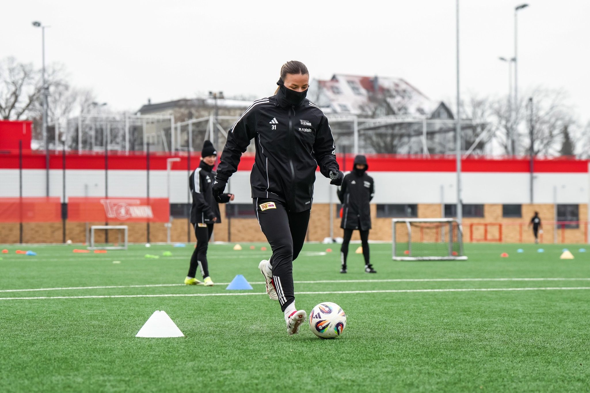 Eine Fußballspielerin in Trainingskleidung dribbelt einen Ball auf einem mit Hütchen markierten Kunstrasenplatz.