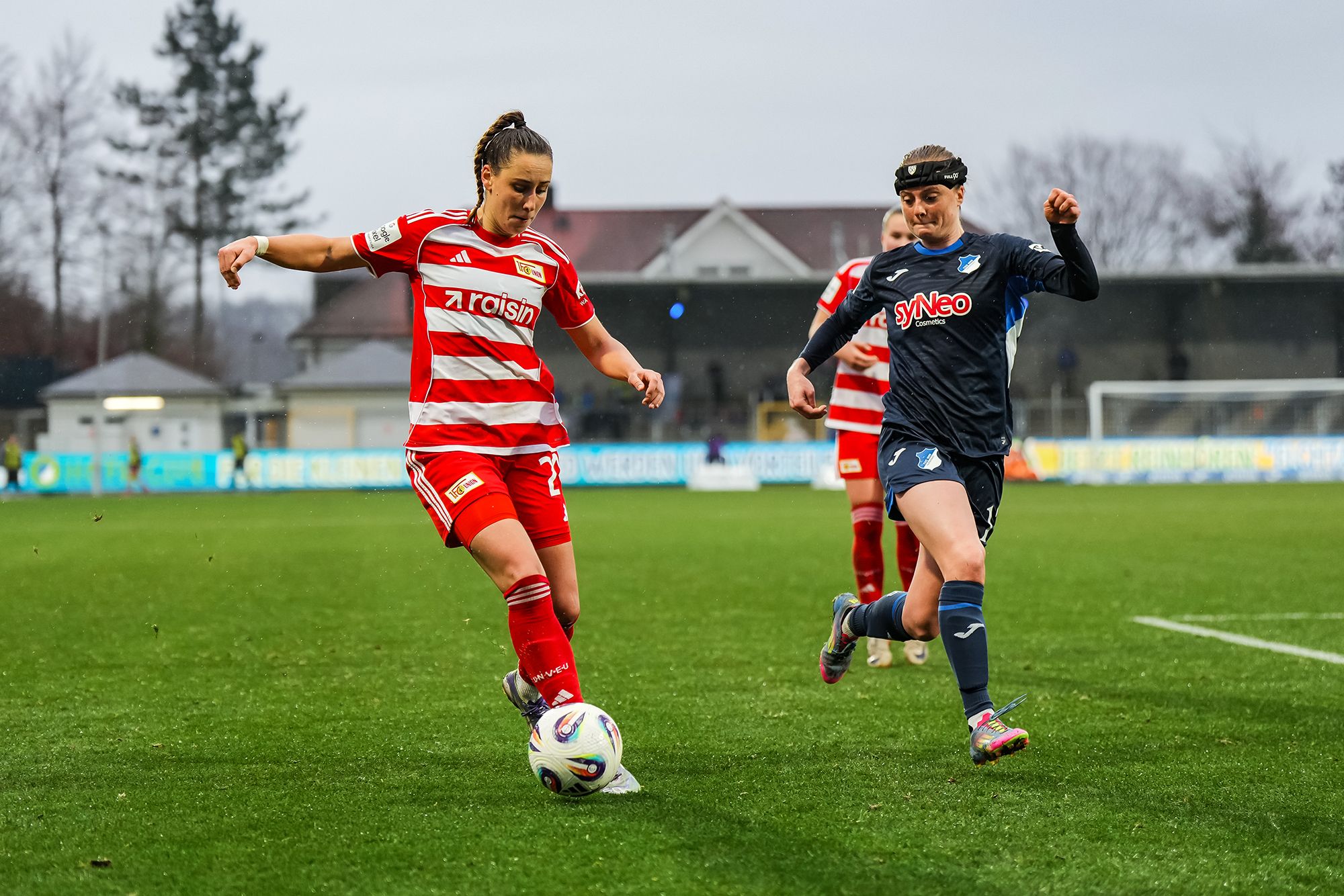 Zwei Fußballspielerinnen im Wettkampf, die eine rote und weiße sowie eine blaue und schwarze Spielkleidung tragen.