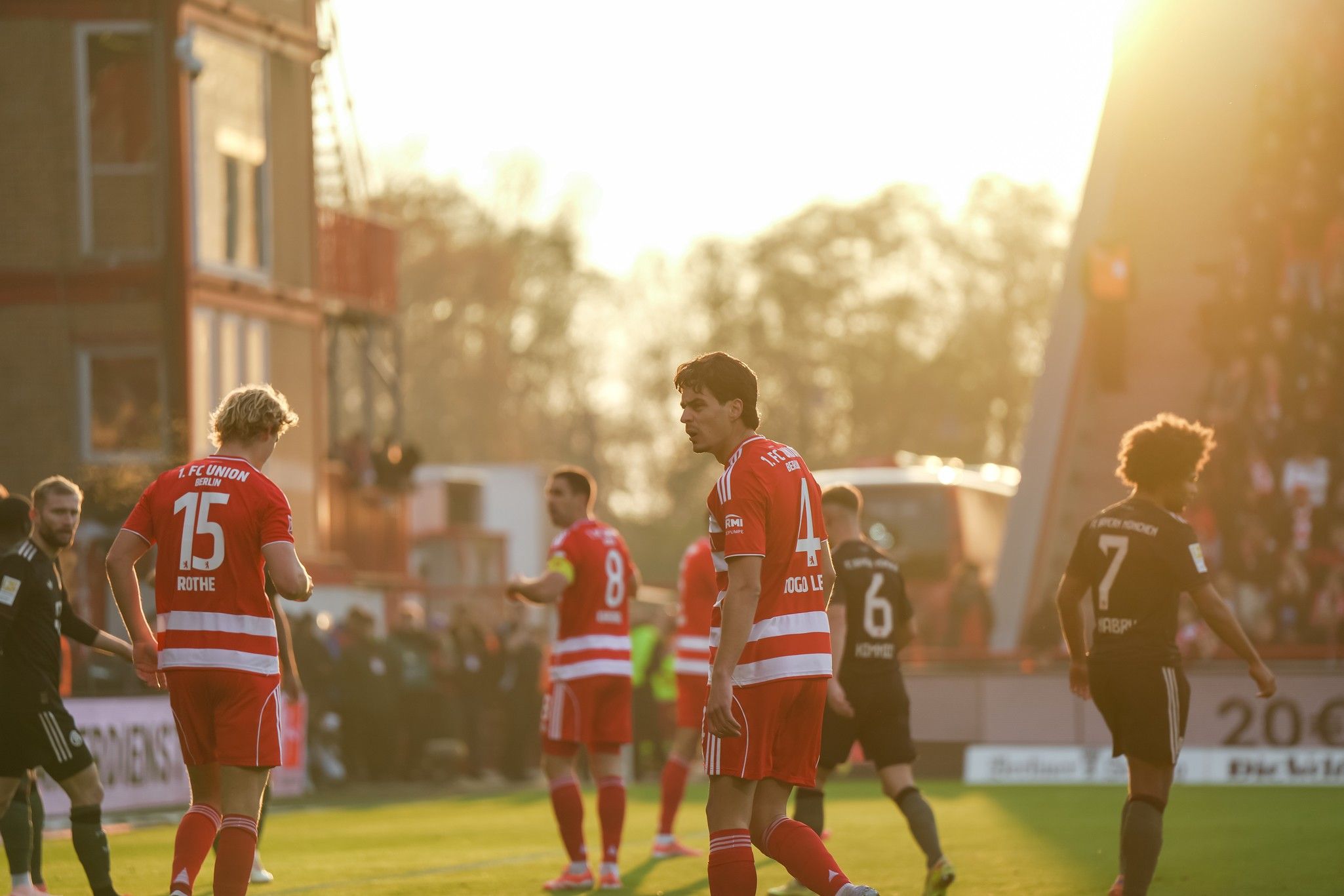 Fußballspiel bei Sonnenuntergang mit Spielern in rot-weiß gestreiften Trikots auf einem Stadionfeld.