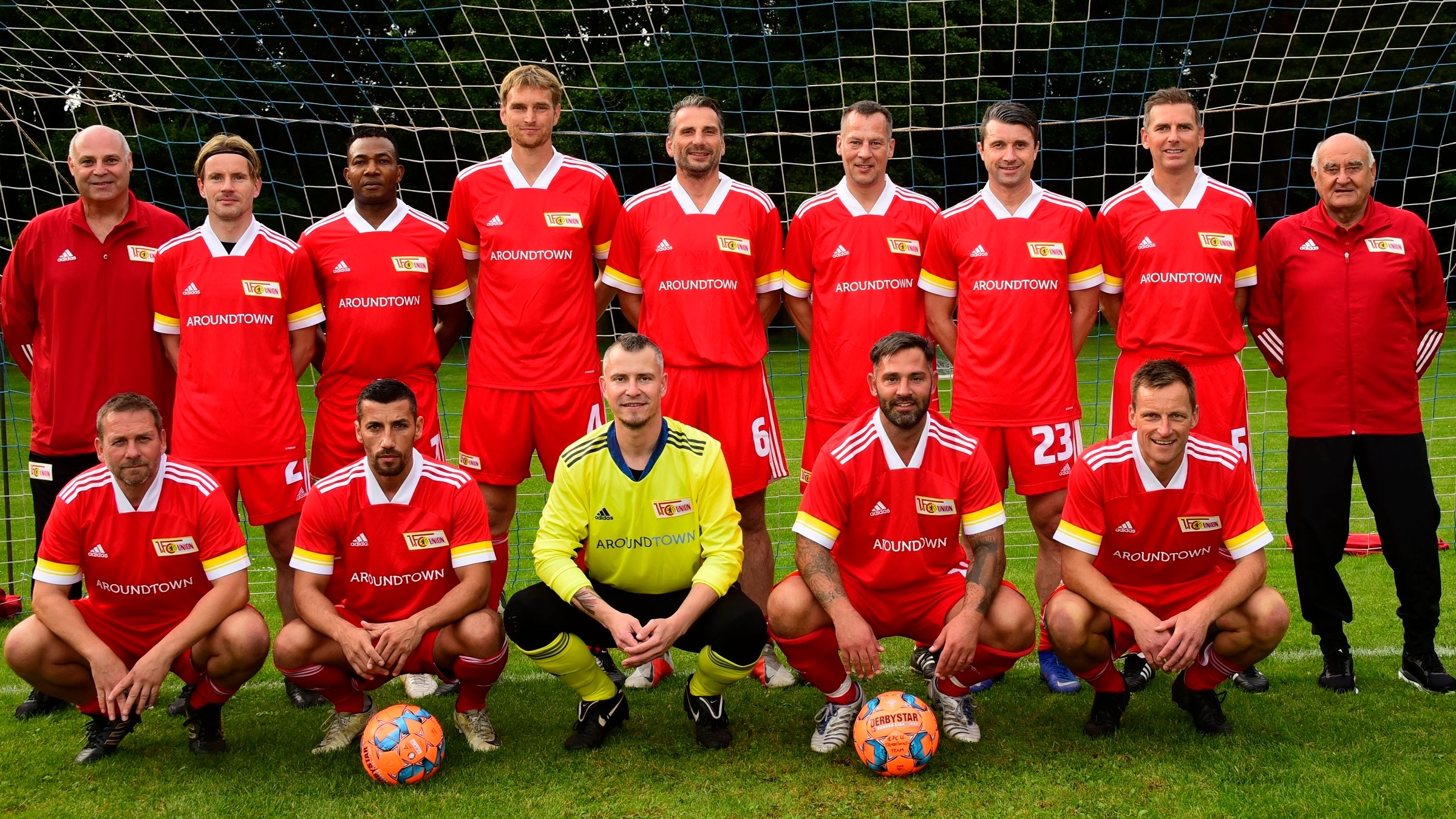 Mannschaftsfoto einer Fußballmannschaft in roten Trikots, auf einem Rasenplatz, vor einem Tor posierend.