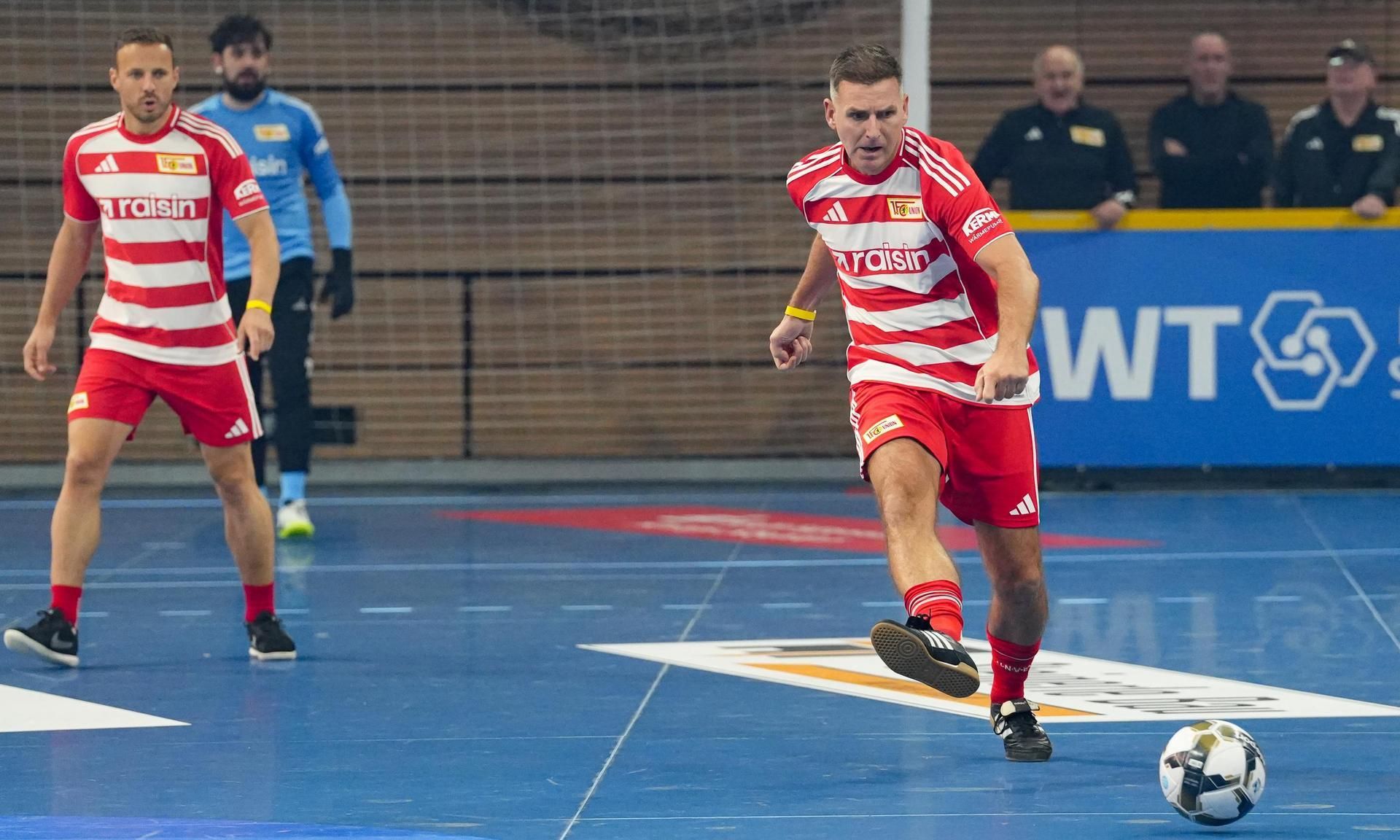 Zwei Fußballspieler in roten und weißen gestreiften Trikots, einer schießt den Ball, der andere steht bereit.