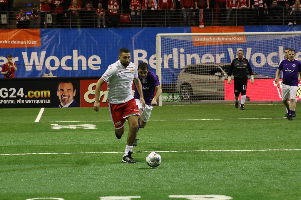 Ein Fußballspieler in weißem Trikot sprintet über das Spielfeld, während ein Gegner ihn verfolgt. Fans sind im Hintergrund sichtbar.