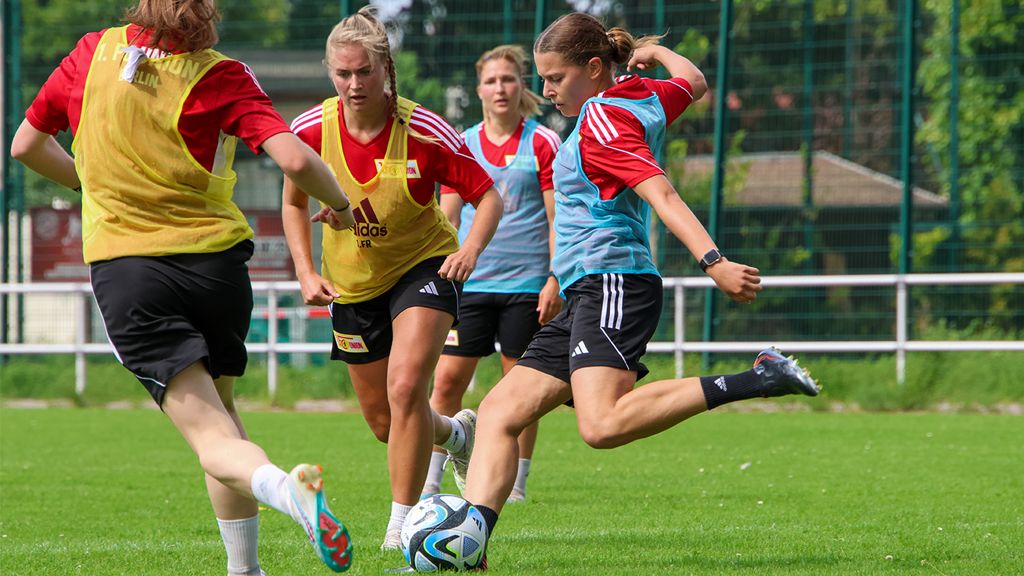 Women's football training on a green field, with players in red jerseys playing and moving with the ball.