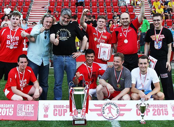 Gruppenshot von Fußballspielern und Betreuern, die mit Pokalen und Medaillen nach einem Turnier posieren.