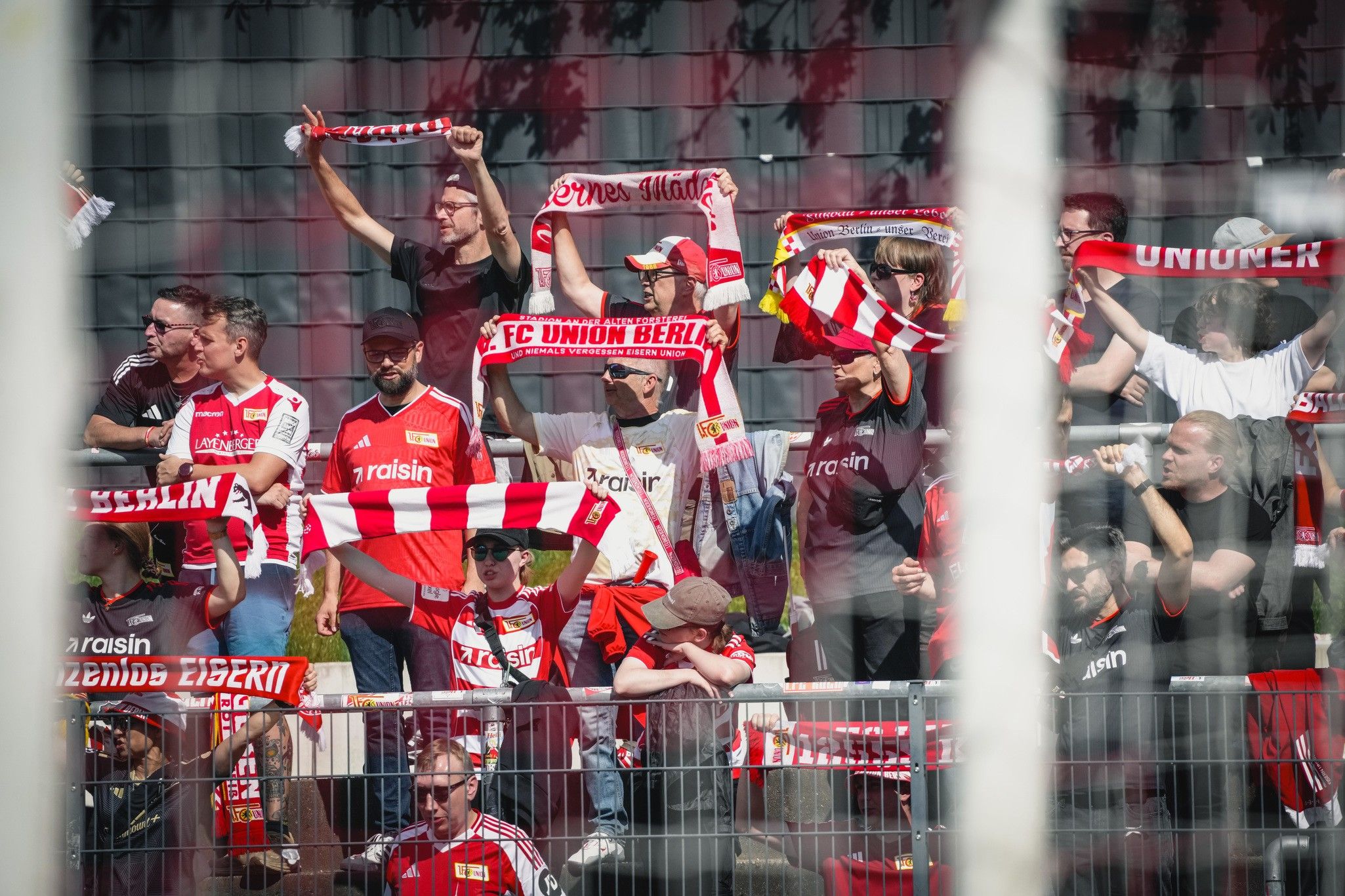 Eine Gruppe von Fans des FC Union Berlin in rot-weißen Trikots, die Schals und Fahnen halten und jubeln.