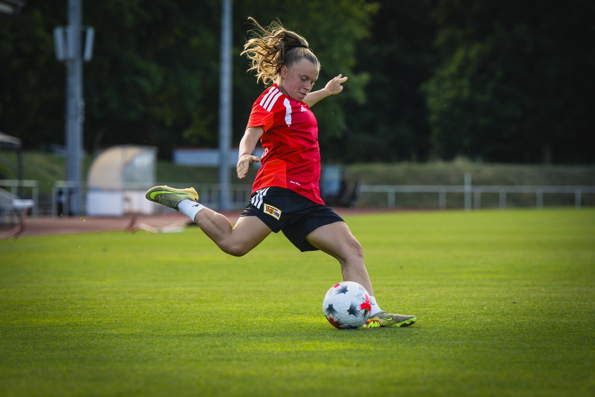 Eine Fußballspielerin in rotem Trikot tritt den Ball auf einem grünen Spielfeld.