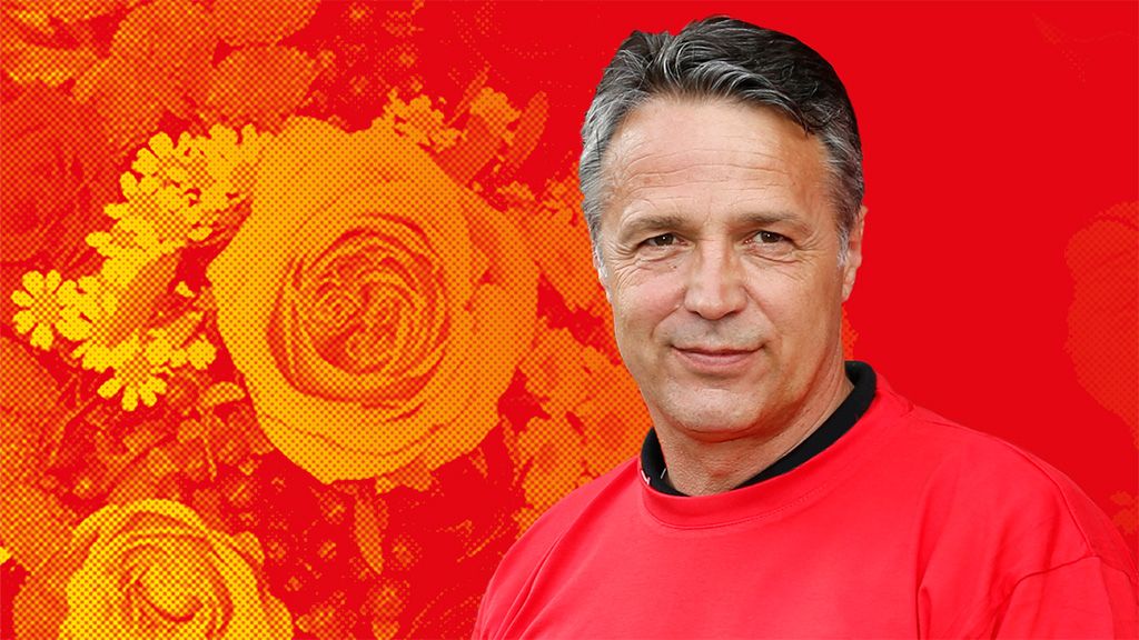 Ein Mann mit grauen Haaren trägt einen roten Pullover, vor einem bunten Hintergrund mit stilisierten Blumenmotiven.