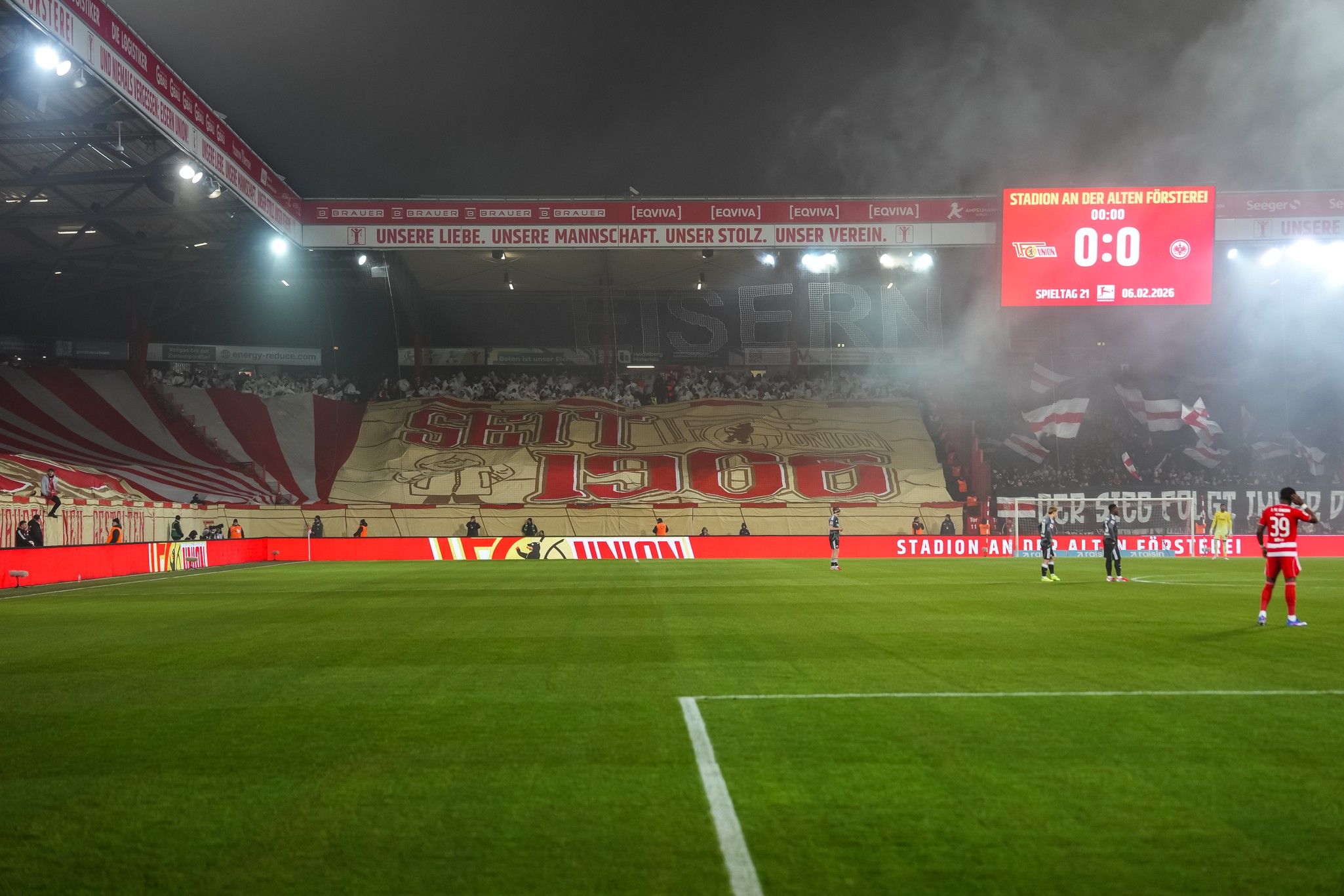 Fanbanner im Stadion mit der Aufschrift "Seit 1900", rauchige Atmosphäre und Spielstand von 0:0 auf der Anzeigetafel.