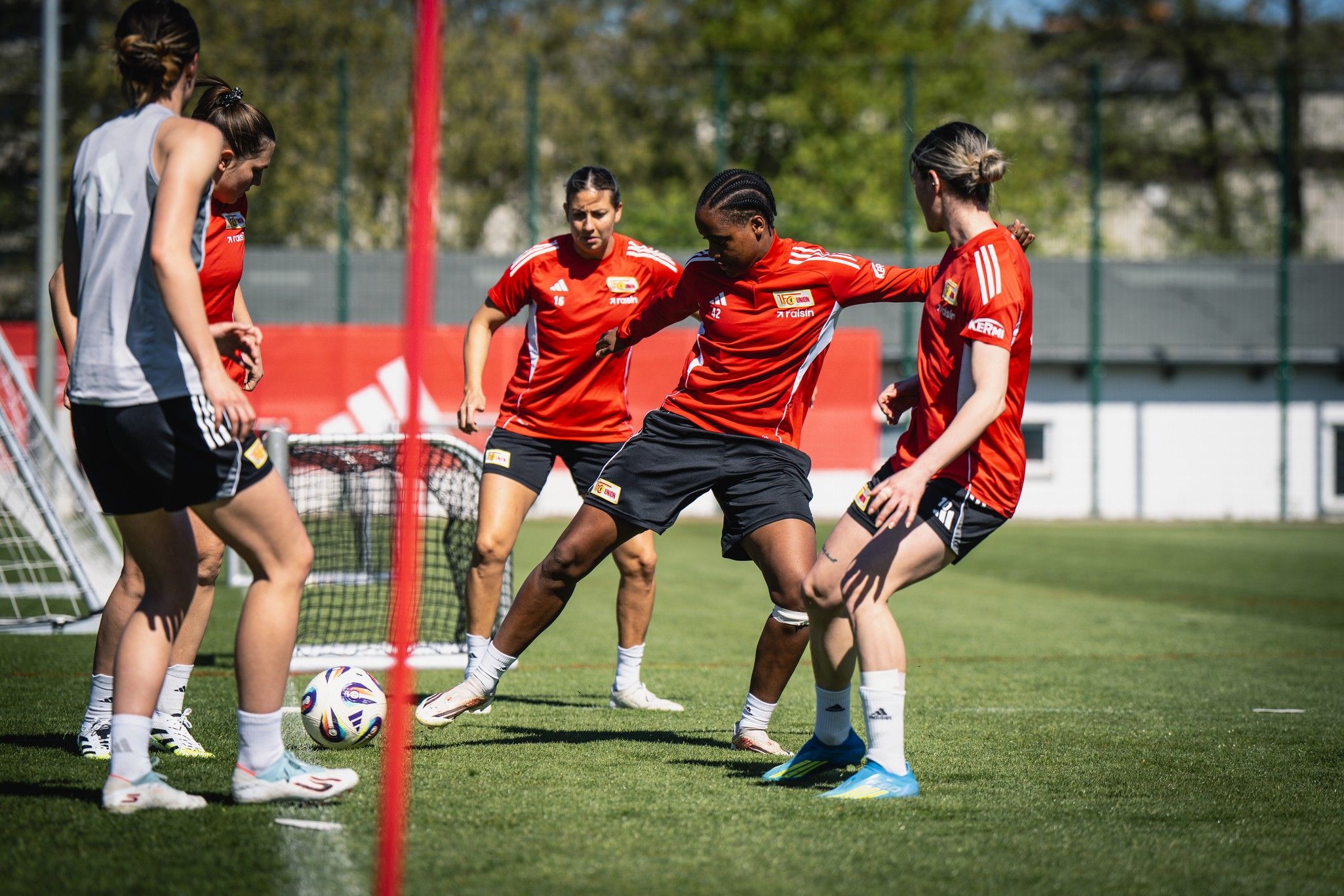 Sechs Fußballspielerinnen in roten Trikots trainieren auf einem Rasenplatz, während sie den Ball umdribbeln.