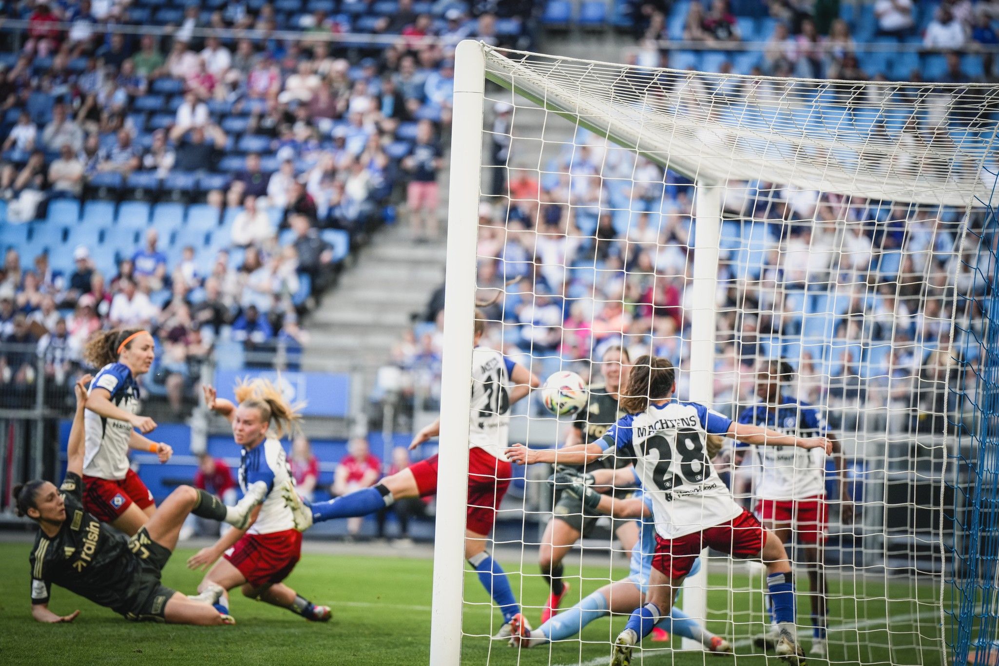 Eine Fußballspielszene mit mehreren Spielerinnen, die um den Ball im Strafraum kämpfen. Torwart in Aktion vor dem Tor.