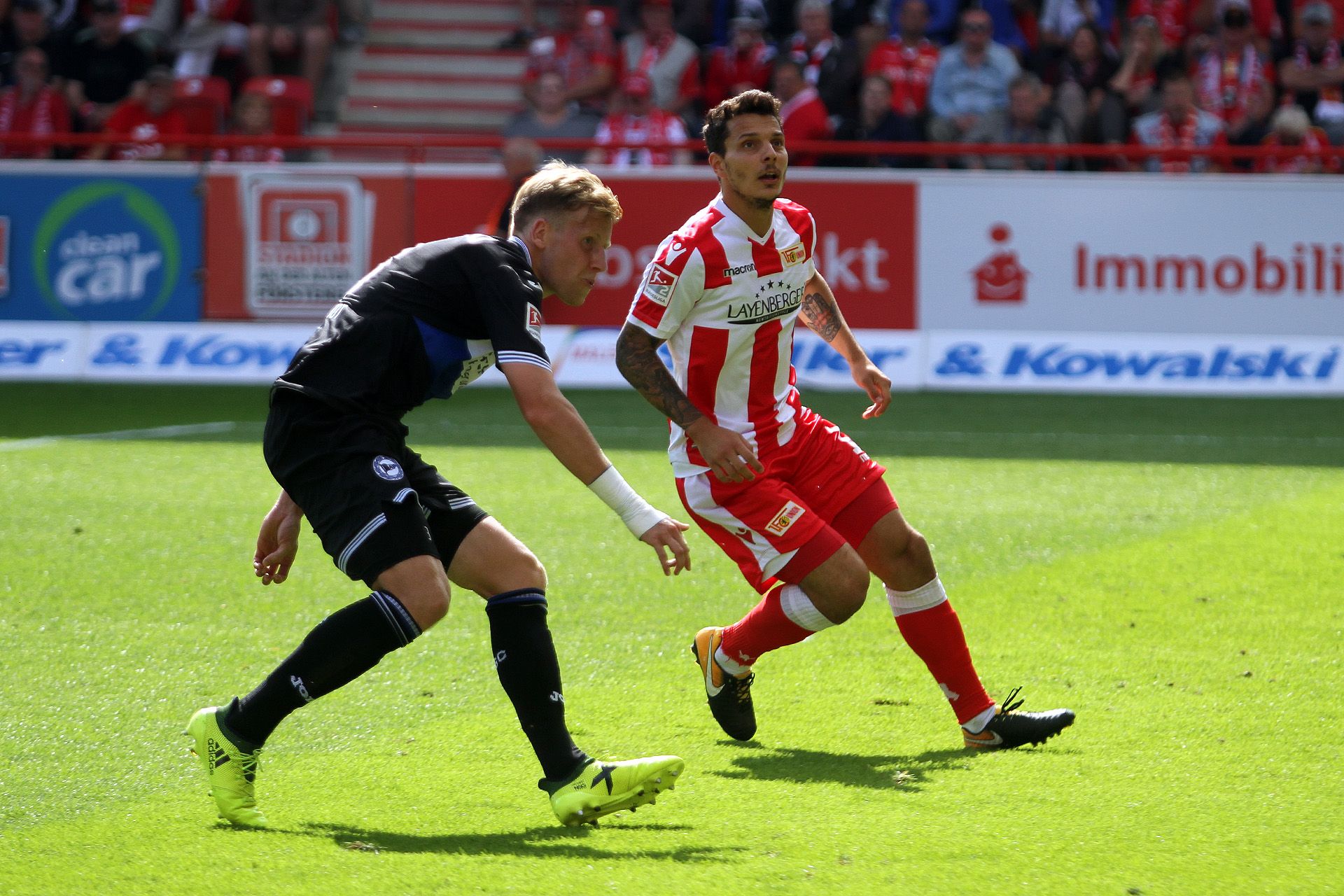Ein Fußballspieler in rot-weißer Uniform dribbelt am Ball vorbei an einem Gegner in schwarzer Torwart-Ausrüstung.
