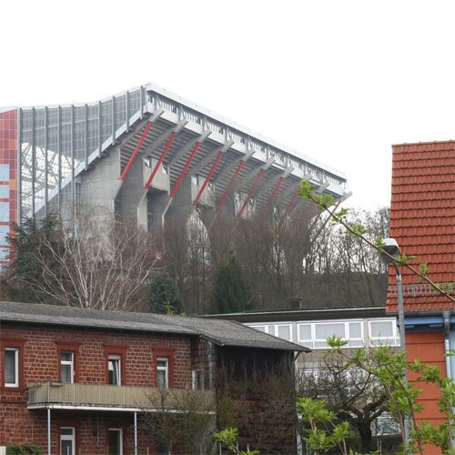 Moderne Stadionarchitektur mit einem Gebäudekomplex im Hintergrund und älteren Häusern im Vordergrund.
