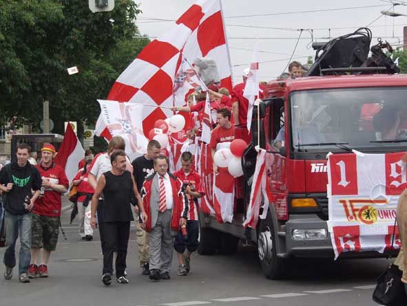 Gruppierung von Fußballfans mit roten und weißen Flaggen und Ballons, die in einer Straßenparade jubeln und feiern.