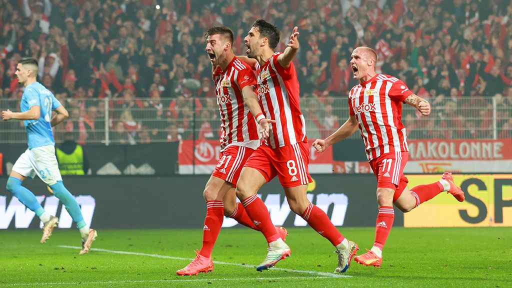 Fußballspieler in roten und weißen Trikots feiern einen Torerfolg vor jubelndem Publikum.