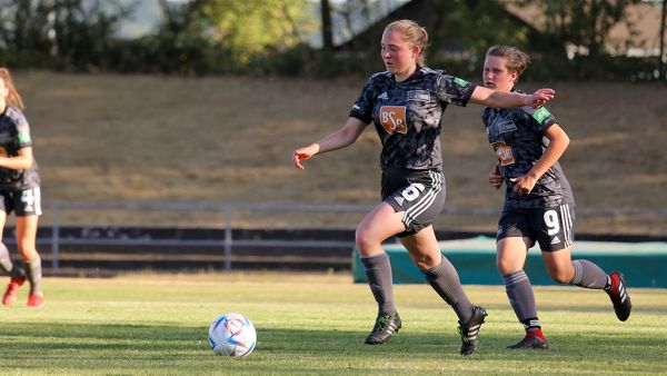 Two female soccer players running on a grass field in sports attire.