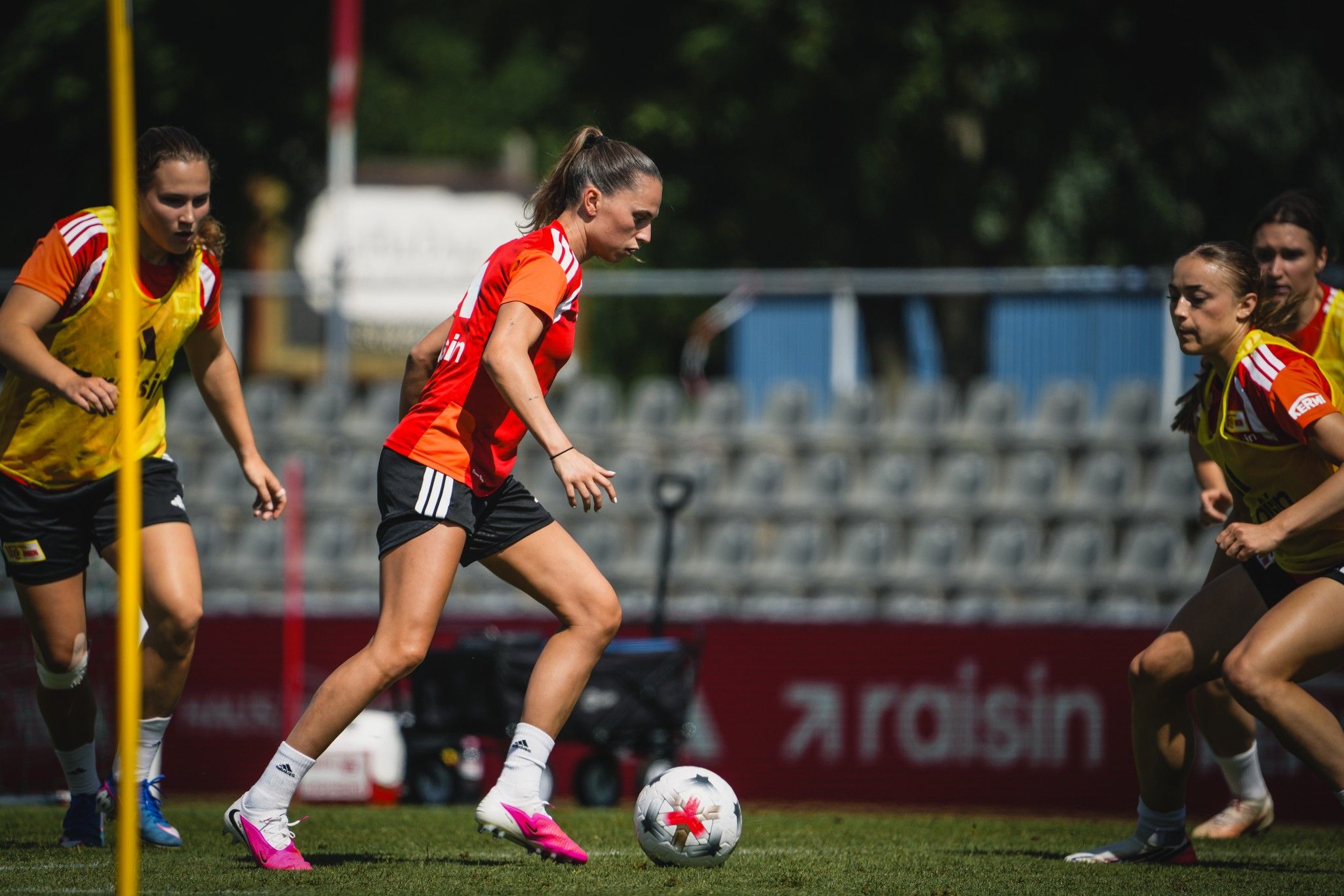 Eine Fußballspielerin dribbelt den Ball während eines Trainings mit Teamkolleginnen auf einem Sportplatz.