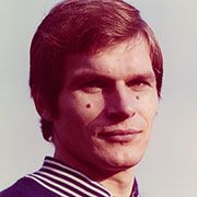 Porträt eines Mannes mit kurzem, braunem Haar und einem leichten Lächeln, bekleidet mit einem sportlichen Oberteil.