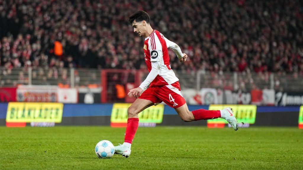 A player in a red and white soccer jersey kicks the ball on the field during a game.